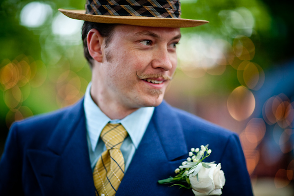 the handsome groom wearing a dark blue suit, a yellow tie with blue and white stripes, a straw derby hat with blue and orange border, and a white floral boutonniere - photo by New Mexico based wedding photographers Twin Lens